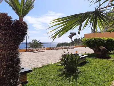 a patio with chairs and a palm tree and the ocean at Hotel Cais da Oliveira in Caniço