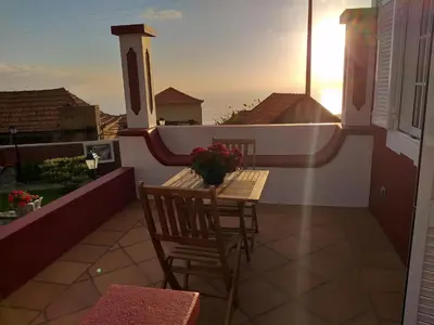 a balcony with a table and chairs and the sunset at the old school in Calheta