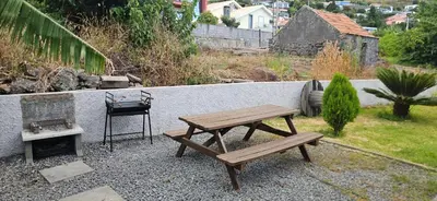 a wooden picnic table and a grill in a backyard at migs'place in Arco da Calheta