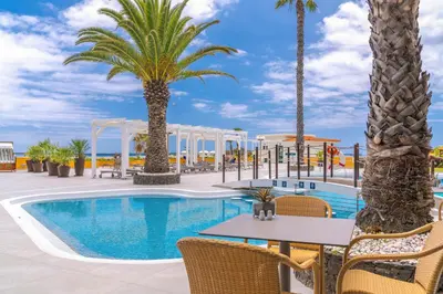 a pool with palm trees and a table and chairs at Sentido Galosol in Caniço