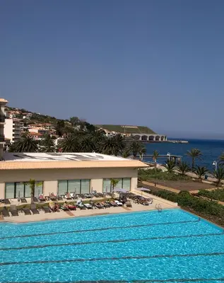 a large swimming pool next to a building and the ocean at Vila Gale Santa Cruz in Santa Cruz