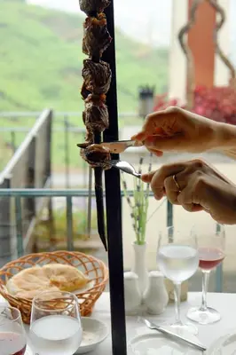 a person is cutting meat on a skewer on a table at Quinta do Estreito in Estreito de Câmara de Lobos