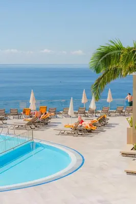 a resort with a pool and chairs and the ocean at Duas Torres Hotel in Funchal