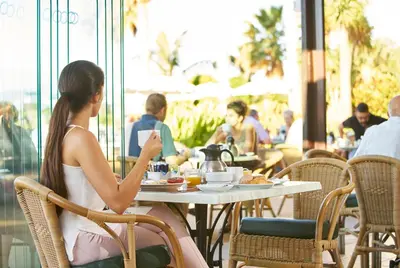 a woman sitting at a table in a restaurant looking at her cell phone at PortoBay Santa Maria - Adults Only in Funchal