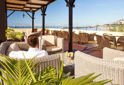 a woman sitting in a chair on a patio overlooking the beach at PortoBay Santa Maria - Adults Only in Funchal
