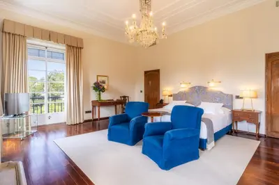 a bedroom with a bed with blue chairs and a chandelier at Quinta da Casa Branca - Small Luxury Hotels of the World in Funchal