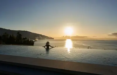 a person sitting in the water in a pool with the sunset at Les Suites at The Cliff Bay - PortoBay in Funchal