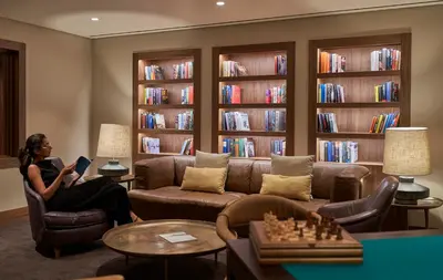 a woman sitting on a couch in a library with a book at Les Suites at The Cliff Bay - PortoBay in Funchal