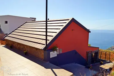 a red building with a roof with the ocean in the background at Palheirinho da Achada in Arco da Calheta