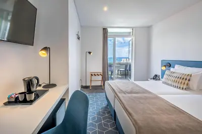 a hotel room with a bed and a desk and a window at Allegro Madeira - Adults Only in Funchal