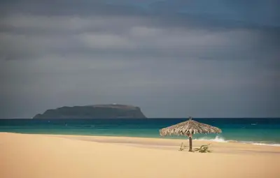 a straw umbrella sitting on a beach near the ocean at Hotel Torre Praia in Porto Santo
