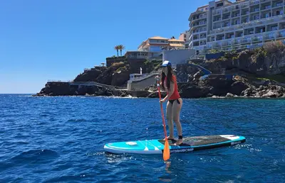 a woman standing on a paddle board in the water at Hotel Royal Orchid in Caniço