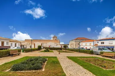 a park with benches and a building with cars at Casa Iemanjá in Vila do Bispo