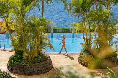 a woman walking by a pool with palm trees at Arcadas III by An Island Apart in Funchal