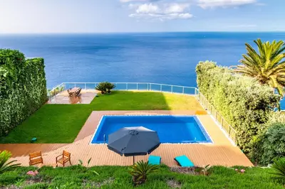a swimming pool with an umbrella and the ocean at Villa Chimera By LovelyStay in Caniço