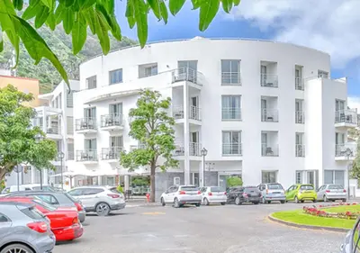 a white building with cars parked in a parking lot at White Waters Hotel in Machico