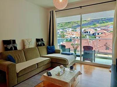 a living room with a couch and a large window at Sunny Little Sister Apartment - 7 min walking from the beach and at 7 min driving from the Airport in Machico