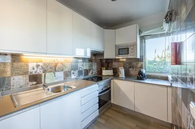 a kitchen with white cabinets and a sink and a window at Pontalaia Apartamentos Turísticos in Sagres
