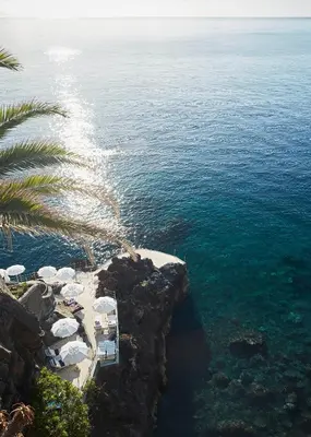 a beach with a palm tree and the ocean at Reid's Palace, A Belmond Hotel, Madeira in Funchal