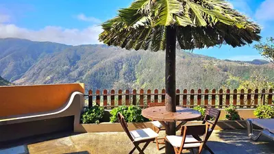 a table and chairs with a palm umbrella on a balcony at Refúgio da Ribeira in Porto Moniz