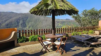 a table with chairs and a palm umbrella on a balcony at Refúgio da Ribeira in Porto Moniz