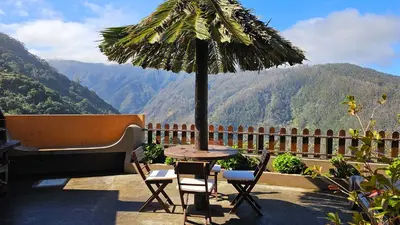 a patio with a table and chairs and a palm umbrella at Refúgio da Ribeira in Porto Moniz