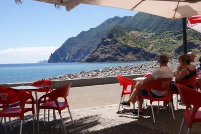 a group of people sitting at a table near the ocean at Hotel Costa Linda in Porto da Cruz
