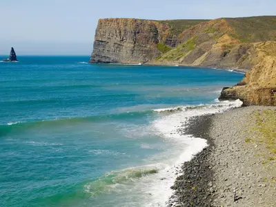 a beach with a rocky shoreline with a lighthouse in the ocean at Hotel Vale Da Telha in Aljezur