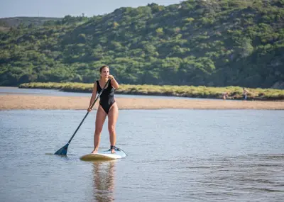 a woman standing on a paddle board in the water at Hotel Vale Da Telha in Aljezur