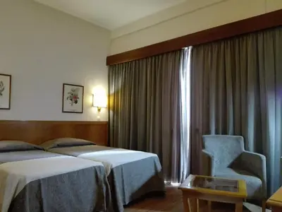 a hotel room with two beds and a chair and a window at Hotel Do Centro in Funchal