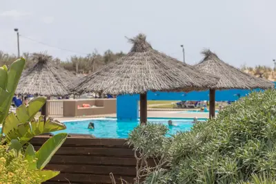 a swimming pool with straw umbrellas on top of it at Vila Baleira Porto Santo in Porto Santo