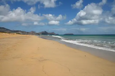 a sandy beach with the ocean and mountains in the background at Vila Baleira Porto Santo in Porto Santo