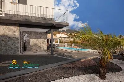 a building with a palm tree next to a swimming pool at OurMadeira - Casa da Rosalina in Calheta