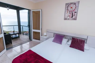 a bedroom with a bed with purple pillows and a balcony at Calheta Holiday Houses in Arco da Calheta