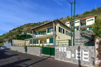 a yellow building with green doors on a hill at Calheta Holiday Houses in Arco da Calheta