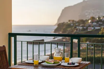 a table with food and drinks on a balcony with the ocean at Vila Formosa I by An Island Apart in Funchal