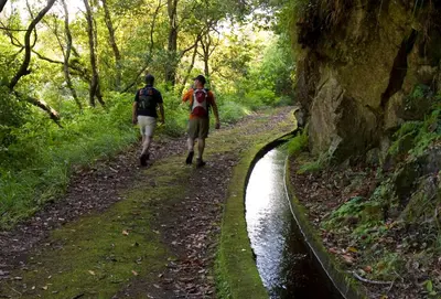 two people walking down a path next to a river at A Casa do Lagar in São Jorge
