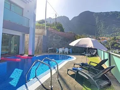 a swimming pool with chairs and an umbrella next to a house at Villa North Sea by LovelyStay in Ponta Delgada