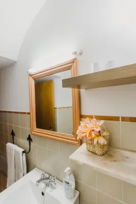 a bathroom with a sink and a mirror and a basket of flowers at Casinha do Paiol in Porto da Cruz