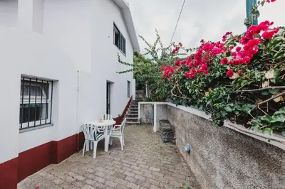 a path leading to a white house with pink flowers at Casinha do Paiol in Porto da Cruz