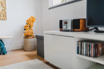 a white living room with a tv and a vase with flowers at O Clube in Porto da Cruz