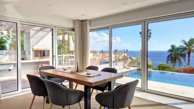 a dining room with a table and chairs and a view of the ocean at Villa Madeira by LovelyStay in Caniço