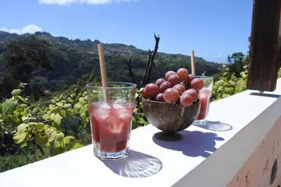 two glasses of drinks on a ledge with a bowl of grapes at Quintinha do Álvaro - Holiday house in Santana