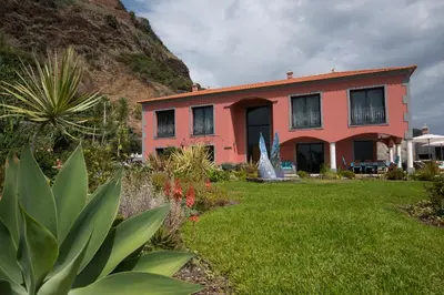 a red house with a garden in front of a mountain at Luxury Ocean Front Villla in Calheta