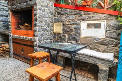 a table and two stools in front of a stone wall at King's House - Centennial House in Arco da Calheta