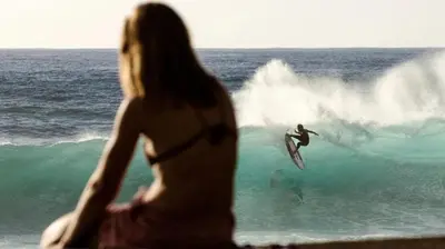 a woman looking at a man on a surfboard in the ocean at King's House - Centennial House in Arco da Calheta