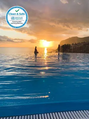 a person standing in the water in the ocean at sunset at Formosa Infinity Pool Apartment in Funchal
