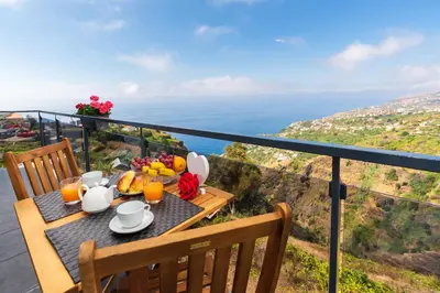 a table with a breakfast of fruit and juice on a balcony at Casa das Abertas in Calheta