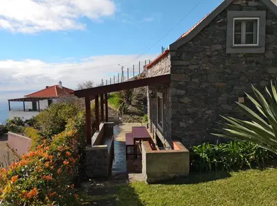 a stone building with a porch with a table and benches at Casa da Manta - Palheiro in Fajã da Ovelha