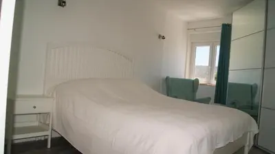 a bedroom with a white bed and two green chairs at Apartamento Próximo da Praia in Luz